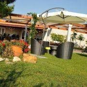 Zona de jardim com mesa sob guarda-sol branco, pérgola em madeira e flores vermelhas.