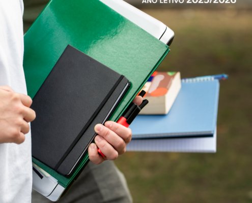 Pessoa de branco segura livros coloridos e materiais de estudo ao ar livre.