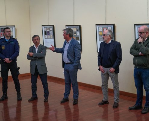 Cinco homens em pé numa sala observando painéis expositivos com rótulos de Vinho do Porto.